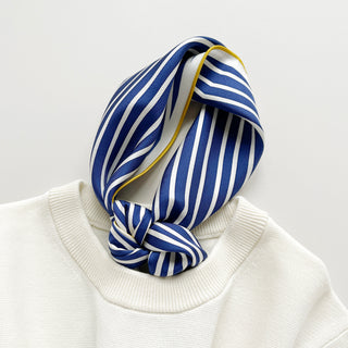 Navy blue and white striped silk scarf with yellow trim elegantly tied around neck of cream sweater, showing luxurious texture and nautical pattern