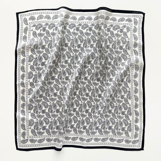 Square silk bandana in black and white with intricate paisley pattern throughout and elegant black border, displayed flat showing luxurious texture
