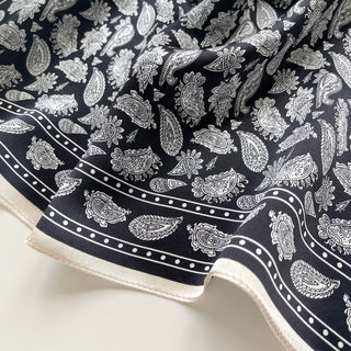 Black and white silk bandana scarf with intricate paisley pattern and dotted border detail, showcasing luxurious fabric texture and elegant cream trim