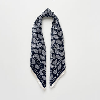 Navy blue silk bandana scarf with white paisley pattern, square design with decorative border, displayed unfolded against white background