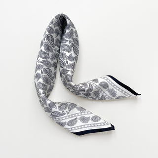Elegant white silk bandana scarf with black paisley pattern and navy border, gently draped to showcase its luxurious texture and classic design.
