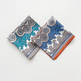 Two folded silk scarves with baroque paisley pattern in blue, turquoise, white, and orange with intricate ornamental borders