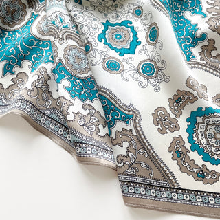 Elegant silk scarf with vintage baroque pattern in turquoise blue and taupe on cream background, featuring ornate medallions and decorative border