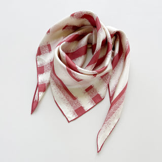 Triangle silk scarf with grapefruit pink striped pattern on cream background, displaying luxurious drape and hand-rolled edges against white surface