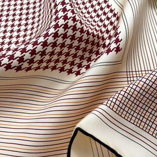 Luxurious silk scarf with deep red and white houndstooth pattern, featuring elegant striped borders and hand-rolled edges on cream background