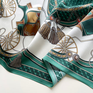 Luxury silk scarf featuring elegant equestrian design with emerald green borders, gold wheels, chains, and decorative tassels on white background, showing lustrous fabric texture.