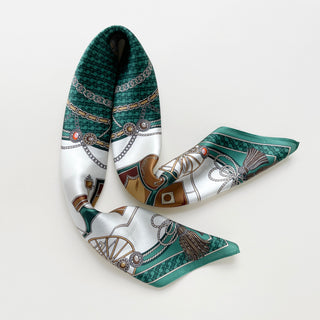 Luxurious silk bandana scarf featuring emerald green and white equestrian pattern with decorative chains, tassels, and ornate details on lustrous satin fabric.