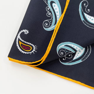 Close-up of black silk scarf with paisley pattern in turquoise, yellow, and red, featuring hand-rolled yellow hem border on premium twill fabric