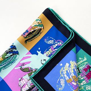 Luxury silk scarf featuring colorful blocks in blue, gold, pink and turquoise with stylized snake print designs, hand-rolled edges and geometric layout