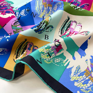 Luxury silk scarf with colorful block design in blue, pink, green, and yellow featuring vibrant snake prints and subtle letter details on shimmering twill fabric