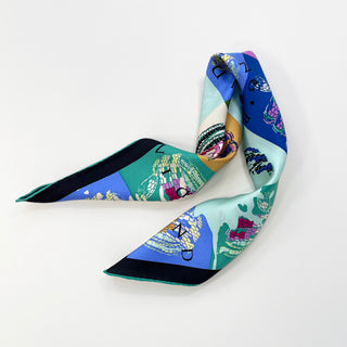 Colorful silk bandana scarf with geometric blocks in blue, green, and gold featuring stylized snake print patterns, displayed in an elegant fold