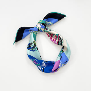Colorful silk bandana scarf tied in a knot featuring vibrant blue, teal, pink, and black geometric blocks with snake print pattern on white background
