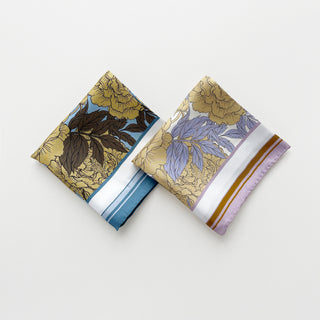 Two folded silk square scarves featuring peonies print on white background in lilac and dusty blue palettes, displaying hand-rolled edges