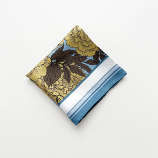 Folded silk scarf featuring light yellow peonies print on light blue background with dusty blue border, displaying hand-rolled edges