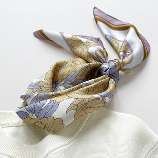 women’s silk neck scarf in light yellow peony print with lilac border, styled in a bow on cream white sweater