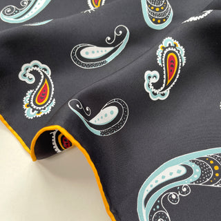 Black silk scarf with colorful paisley pattern featuring teal, orange, and red motifs, showing luxurious texture and orange hand-rolled edge