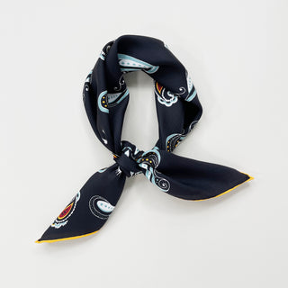 Black silk neckerchief tied in classic knot featuring paisley pattern with light blue, white, and orange accents against deep navy background