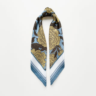 Luxury silk scarf featuring light yellow peonies print on light blue background with dusty blue border, displayed in elegant drape