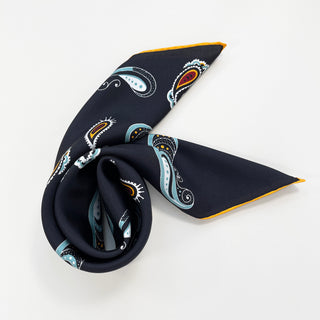 Black silk scarf with colorful paisley pattern featuring blue, orange, and white designs, folded elegantly with yellow edge trim on white background