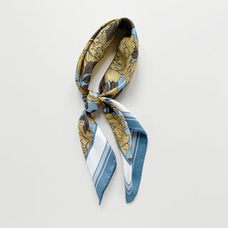 Luxury silk scarf featuring light yellow peonies print on light blue background with dusty blue border, elegantly tied in a loose knot