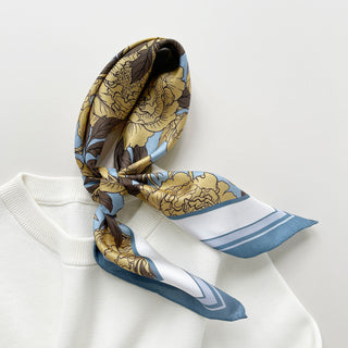 Luxury silk scarf featuring light yellow peonies print on light blue background with dusty blue border, styled in a knot on a white garment