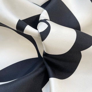 Close-up of luxurious black and white silk scarf featuring elegant camellia flower pattern with smooth hand-rolled edges and lustrous twill texture