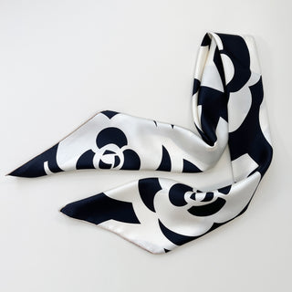 Elegant black and white silk scarf with camellia flower pattern, draped to display its luxurious sheen and hand-rolled edges