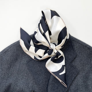 Elegant black and white silk scarf with camellia pattern tied stylishly around neck, displayed on dark gray wool coat