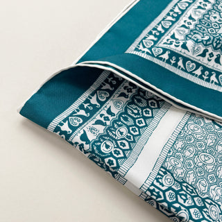 Luxury teal silk scarf with white hand-rolled edges featuring intricate bird and floral patterns in white motifs against turquoise background