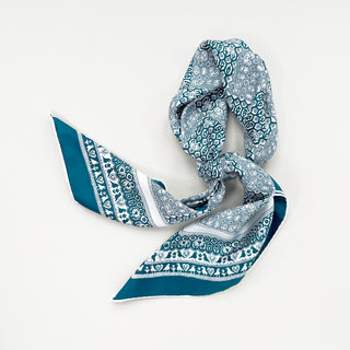 Teal Heritage Grace silk scarf with intricate white patterns featuring birds and floral motifs, elegantly tied against white background.