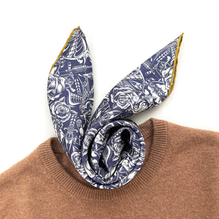 Ink blue silk scarf with white gothic rose pattern and mustard yellow hand-rolled edges, elegantly styled on a camel sweater