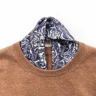 Ink blue silk scarf with white gothic rose pattern elegantly draped inside the collar of a camel sweater, showing detailed floral design.