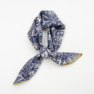 Ink blue silk scarf with white gothic rose pattern, tied in a stylish knot showcasing yellow hand-rolled edges against white background