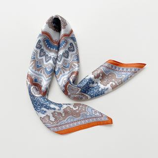 Silk scarf with intricate baroque pattern in blue, orange and beige tones, featuring ornate paisley designs and decorative orange border on luxurious fabric.
