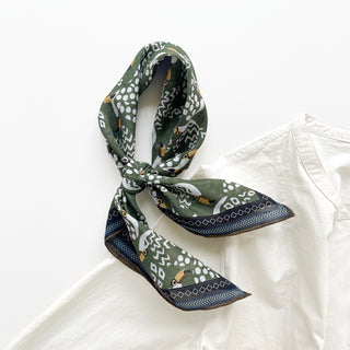 Organic cotton-silk scarf in green with toucan print and understated jacquard texture, elegantly tied in a loose knot, paired with a cream white turtle neck shirt