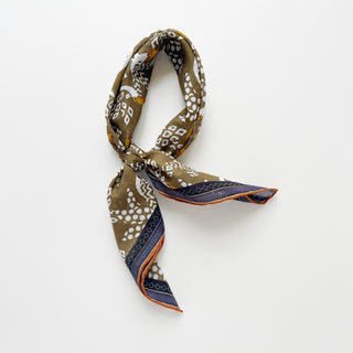 Organic cotton-silk scarf in mustard ochre with toucan print and understated jacquard, featuring contrast border and hand-rolled edges, elegantly tied in a loose knot