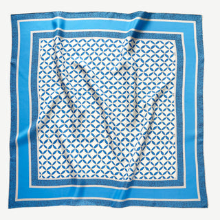 Flat lay of 90x90cm silk scarf with geometric blue petal print and striped border, hand-rolled edges, made of double-sided printed silk twill.