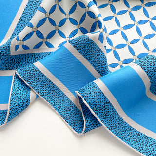 Close-up of women’s silk scarf with blue petal pattern on a light grey base, hand-rolled edges, and smooth silk twill texture.