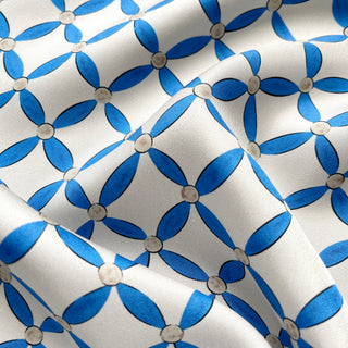 Close-up of women’s silk scarf with blue petal pattern on a light grey base, smooth silk twill texture.