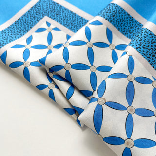 Close-up of women’s silk scarf with blue petal pattern on a light grey base, smooth silk twill texture.
