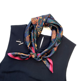 Luxurious vintage silk scarf with navy background, ornate floral patterns in teal, gold and red, tied elegantly on a black garment with pink border trim