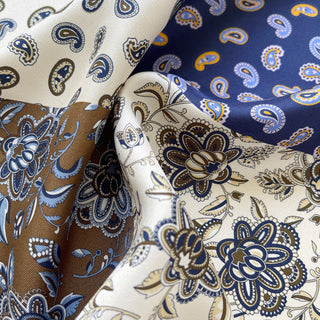 Close-up of mulberry silk men’s neckerchief showing detailed paisley and floral patterns in blue, olive brown and cream.