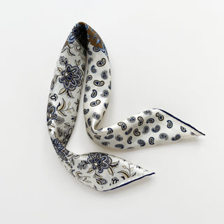 Navy floral and paisley patterned men's silk scarf on a cream white background showing navy hand-rolled finish