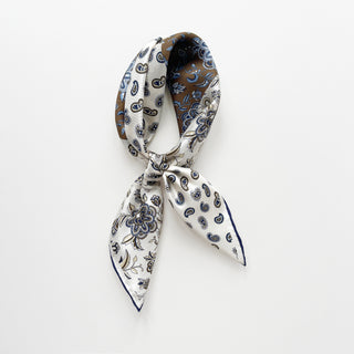 men's silk neckerchief with paisley and floral patterns in cream and olive brown with navy blue hand-rolled edges tied into a knot on a white background