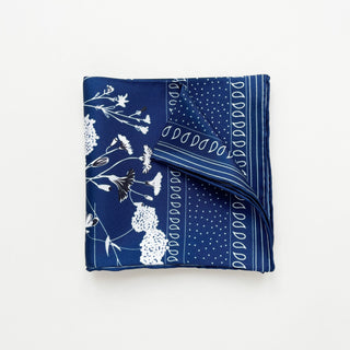 Blue Kyoto Bloom silk scarf featuring elegant white botanical floral pattern with polka dots and decorative border, folded neatly showing texture