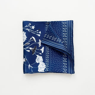 Square navy blue silk scarf with white floral pattern, polka dots, and decorative border, folded to display hand-rolled edges