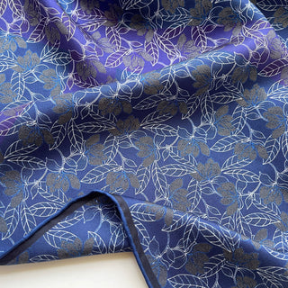 Close up of a men’s silk neckerchief scarf 53cm, double-sided blue and purple floral print with hand-rolled edges, luxury square accessory