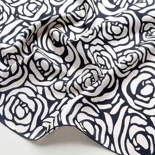 Close up of charcoal black and cream white silk scarf  with a rose print design, showing luxurious fabric texture and hand-rolled edge on a light grey background