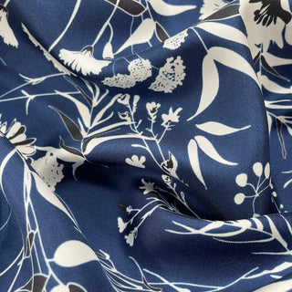 Deep blue silk scarf with elegant white floral pattern, featuring luxurious twill texture and flowing fabric folds showcasing the hand-rolled quality