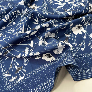 Blue silk scarf with white botanical print featuring delicate flowers and leaves, finished with decorative border pattern, draped to show luxurious silk twill texture